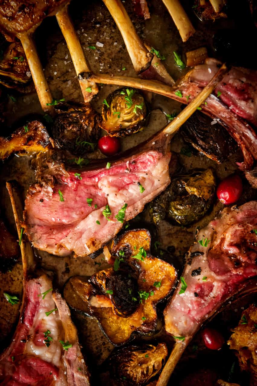 Lamb chop sliced on a board to show rare center with other chops around over roasted squash.