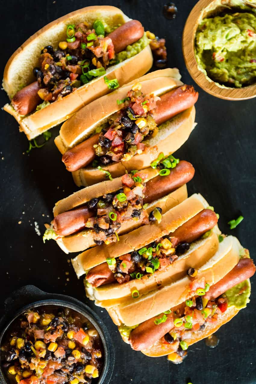 These hot dogs are lined up and loaded with pineapple salsa. Just spoon on some of that delicious guac, and we are ready to chow down!