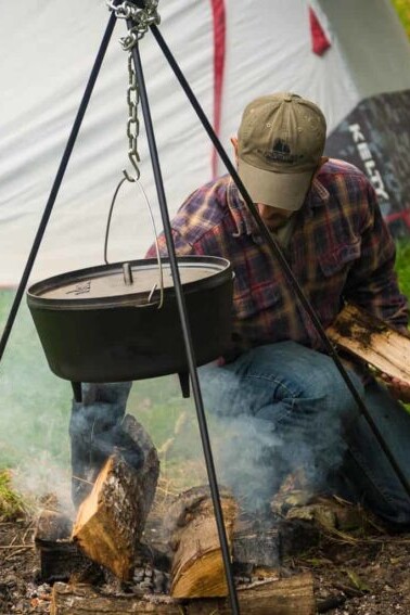 A man cooking lamb over a fire in front of a tent.