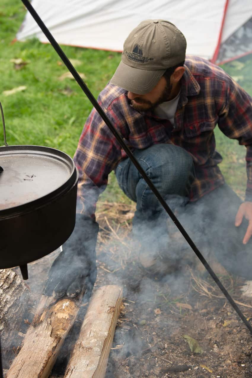 A man is grilling lamb on a campfire in front of a tent.