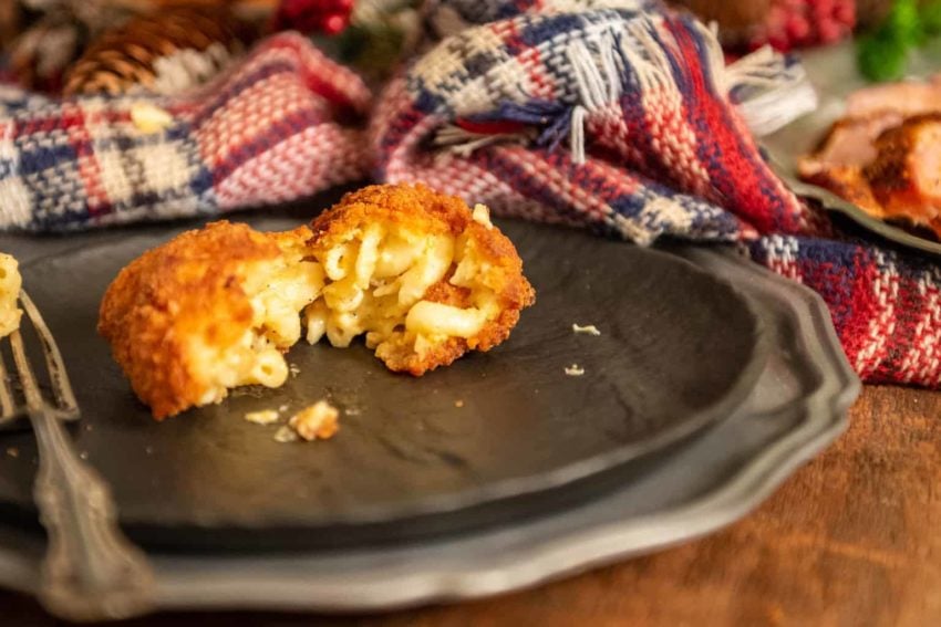 Deep fried macaroni and cheese on a black plate, split apart by a fork