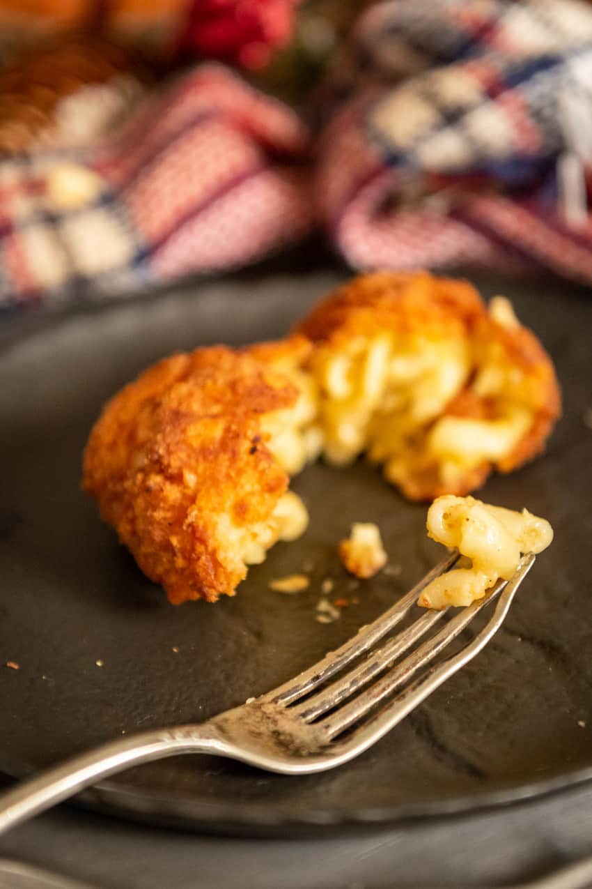 Deep fried macaroni and cheese ball broken apart with a bite of elbow pasta on the end of a fork