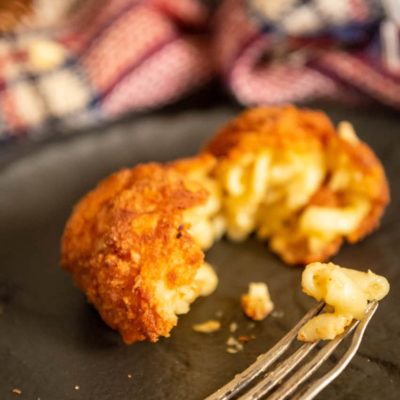Fried Macaroni and Cheese that has been pulled apart with a fork on a black plate.