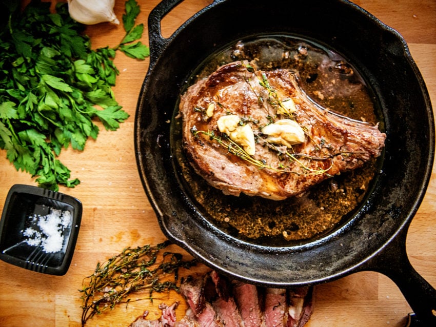 A bone in seared ribeye in a skillet with garlic and butter melted in the drippings