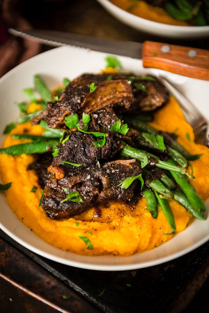 Close up of meaty slow cooker short ribs over pureed veggies and green beans.