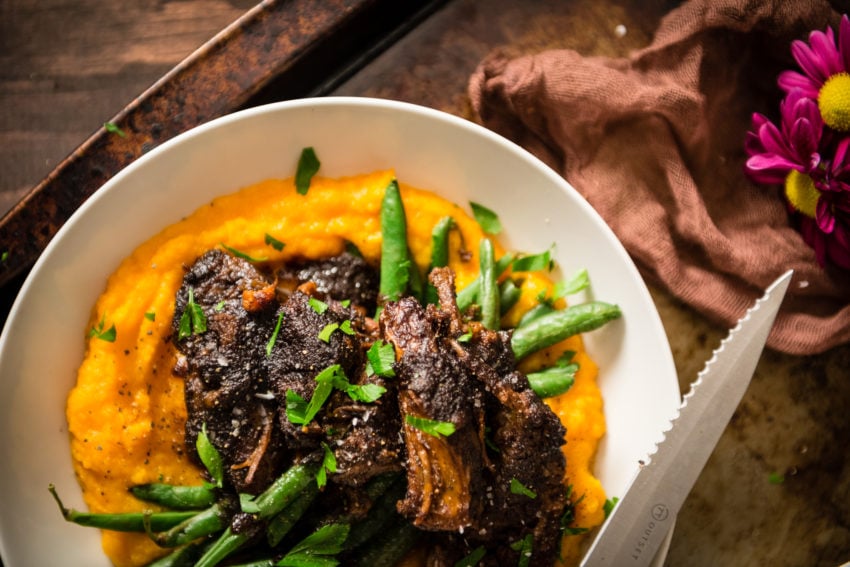Slow cooker short ribs plated in a bowl over sweet potato puree and green beans.