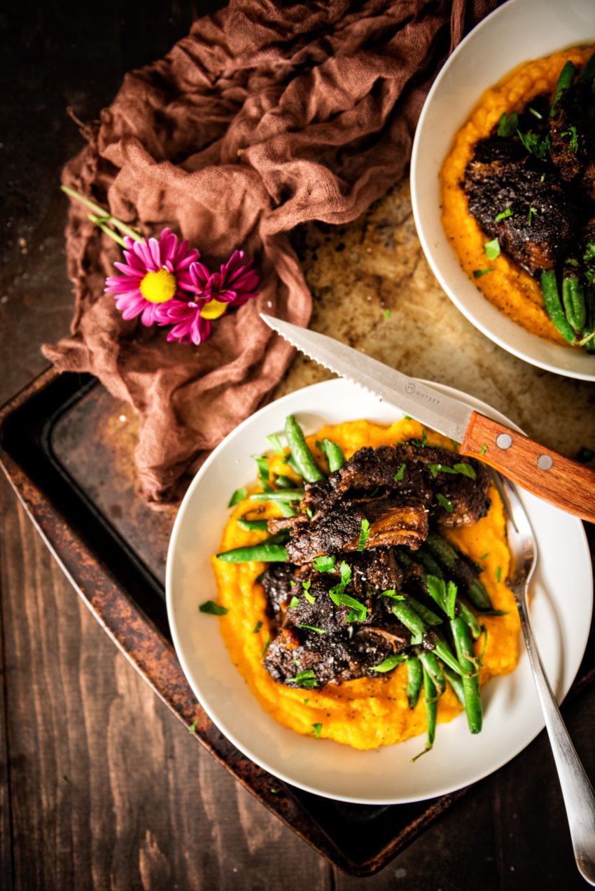 Overhead shot of bowls with potato puree, green beans, and braised short ribs. 