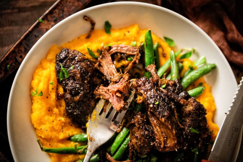 Overhead shot of fork with shredded beef rib meat hanging off it over a bowl of meat and sweet potatoes. 