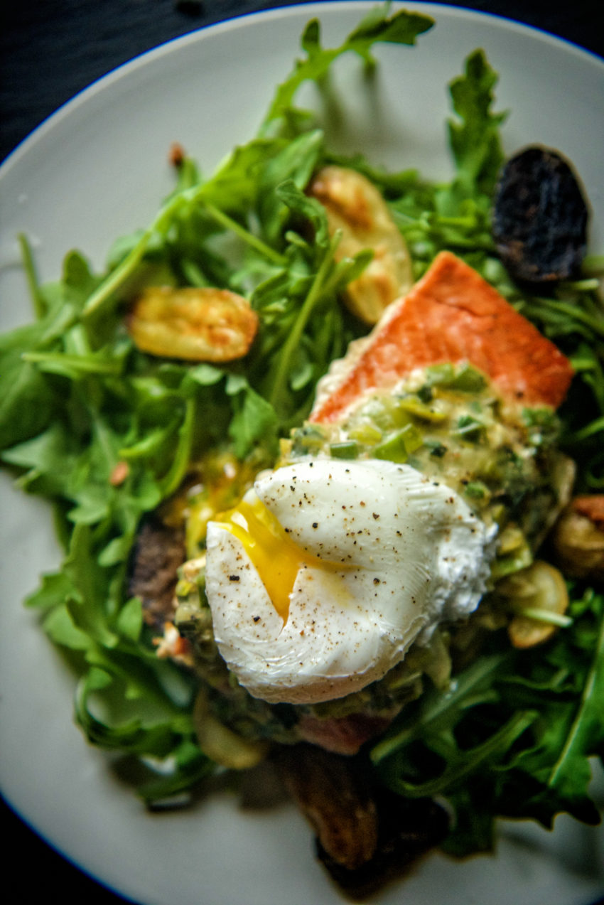 Overhead shot of a salad with pan seared salmon on top and a broken poached egg. 