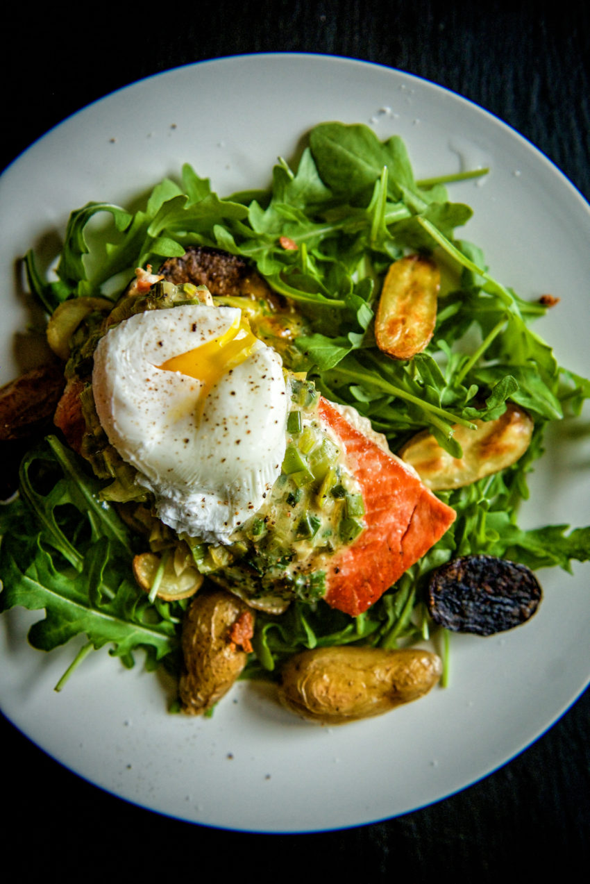 Beautifully seared fish peaking out overtop a colorful bed of greens. 