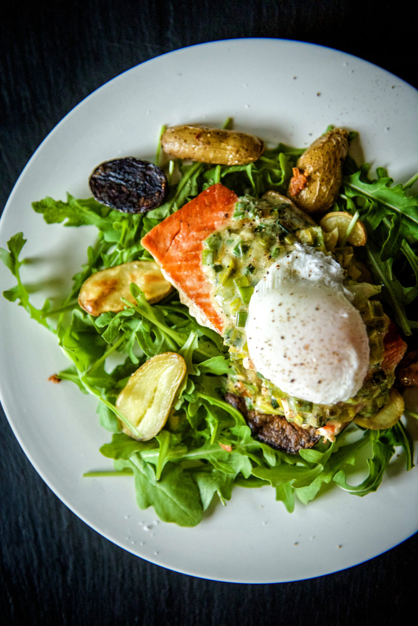 overhead shot of pan seared salmon on a vibrant bed of arugula, with creamed leeks and a poached egg.