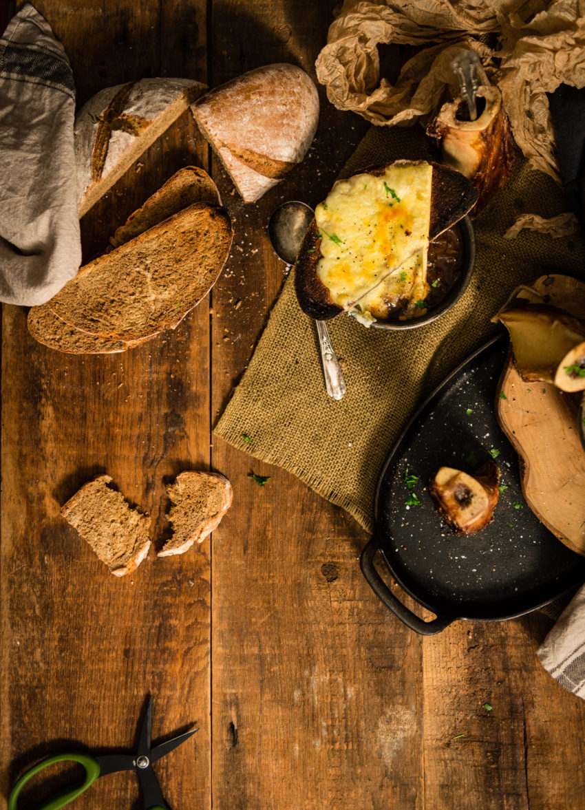 Overhead shot of a wooden table with sliced bread, melted cheese and bowls of soup.