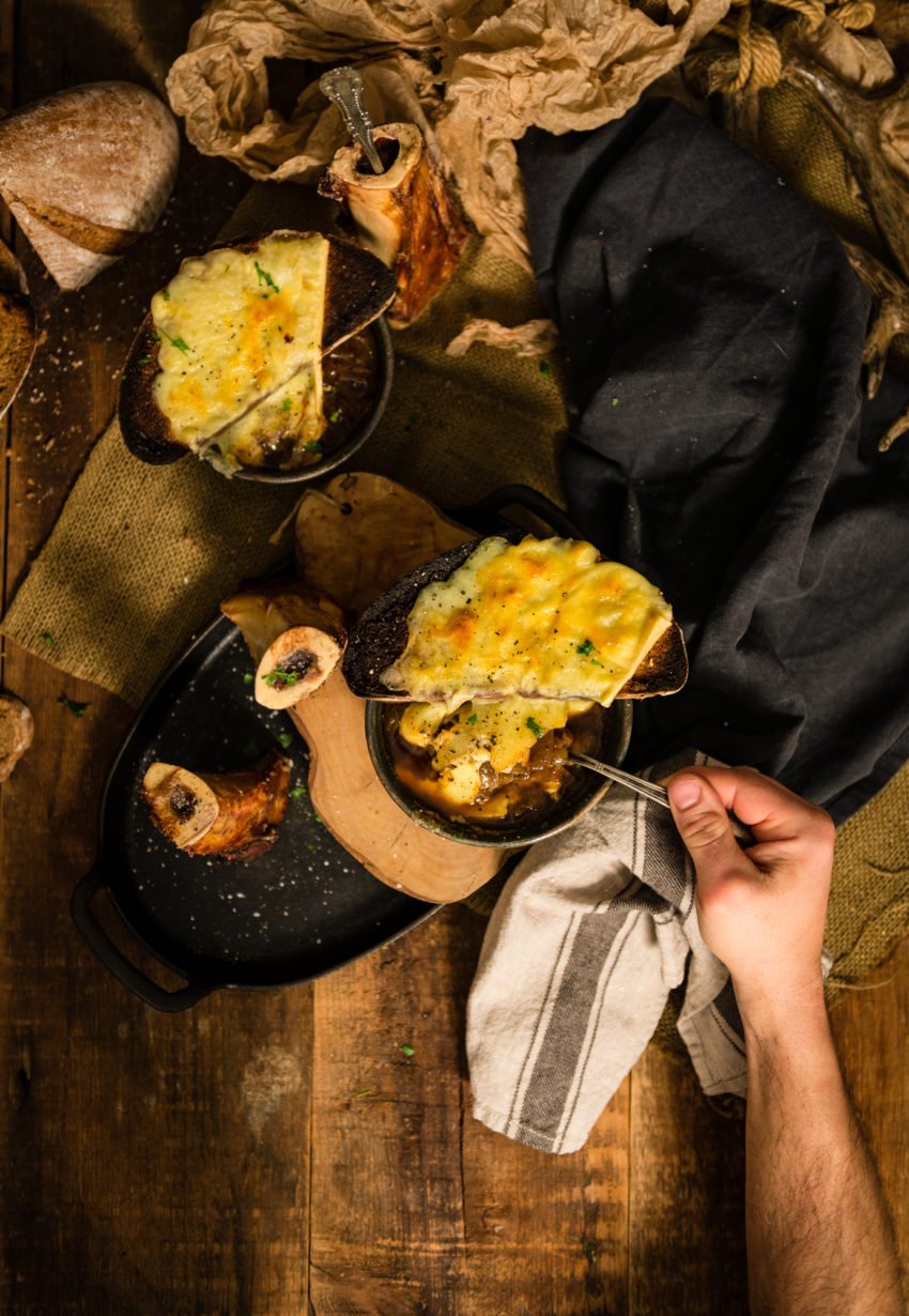 Hand reaching in with a spoon to a bowl of comforting onion soup. 