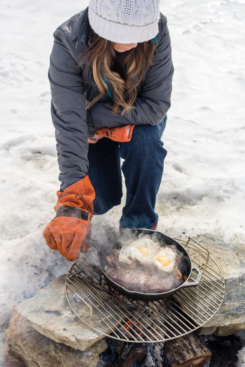 Woman grilling steak over campfire.