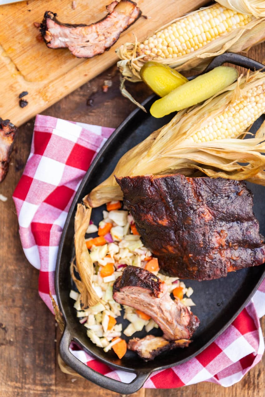 Smoked ribs on a platter with grilled corn and slaw. 