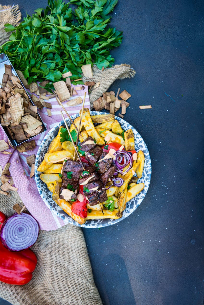 Grilled beef heart kabob recipe over thick cut potatoes with a simple sauce and grilled onions and peppers on a simple background with wood chips and herbs