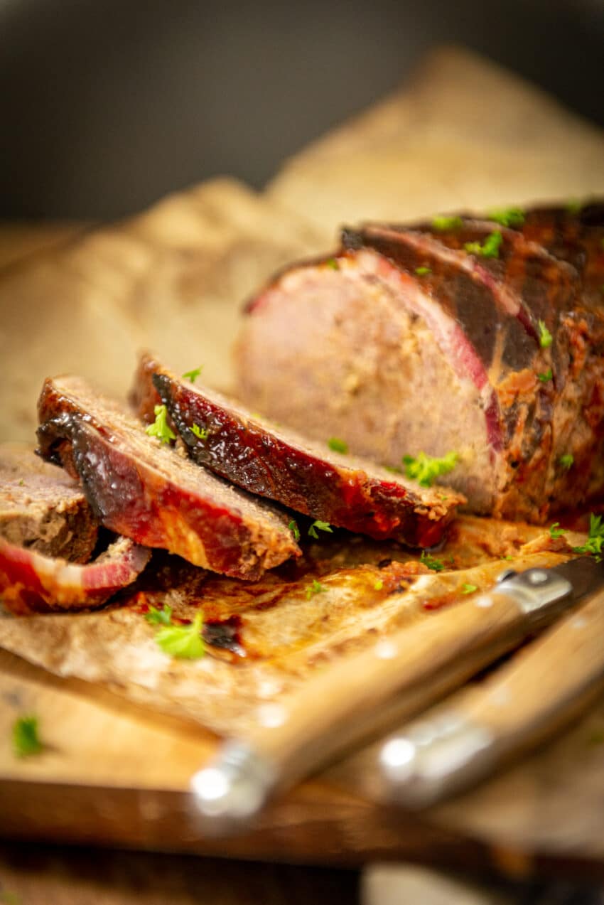 Close up of slices of bacon wrapped meatloaf showing crispy cooked bacon outside the loaf, garnished with parsley. 