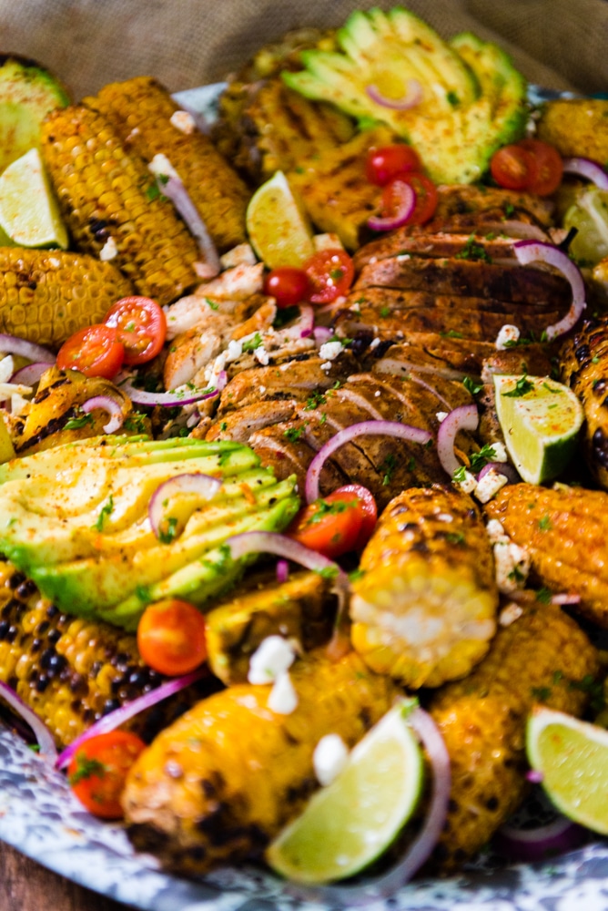 Close up of huge plate filled with smoked chicken breast sliced for serving and surrounded by veggies.