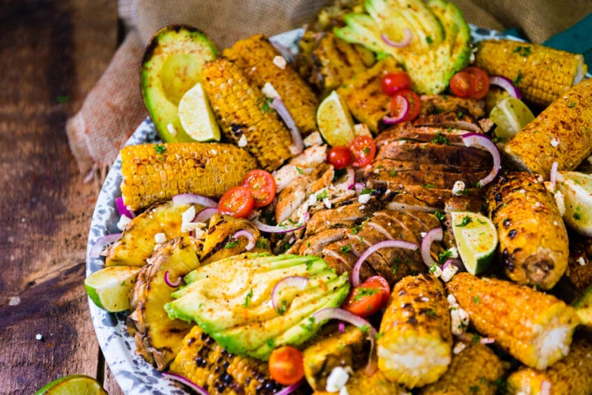 Cooked chicken sliced thin on a huge platter of grilled produce. 