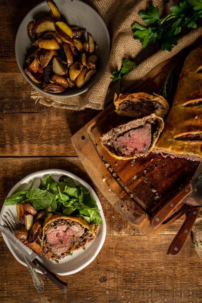 Sliced beef wellington on a plate with greens and potatoes 