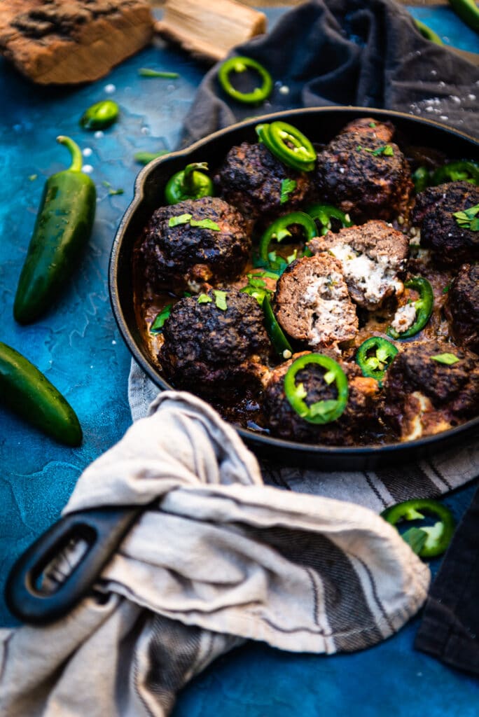 smoked meatballs in a cast iron skillet with one cut open to show the jalapeon popper filling
