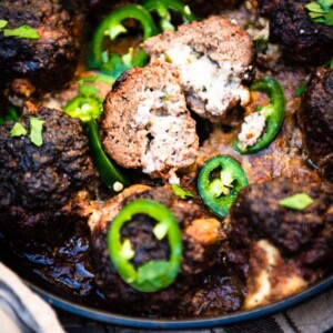 Smoked jalapeno popper meatball in skillet sliced in half to show cream cheese filling with sliced jalapenos