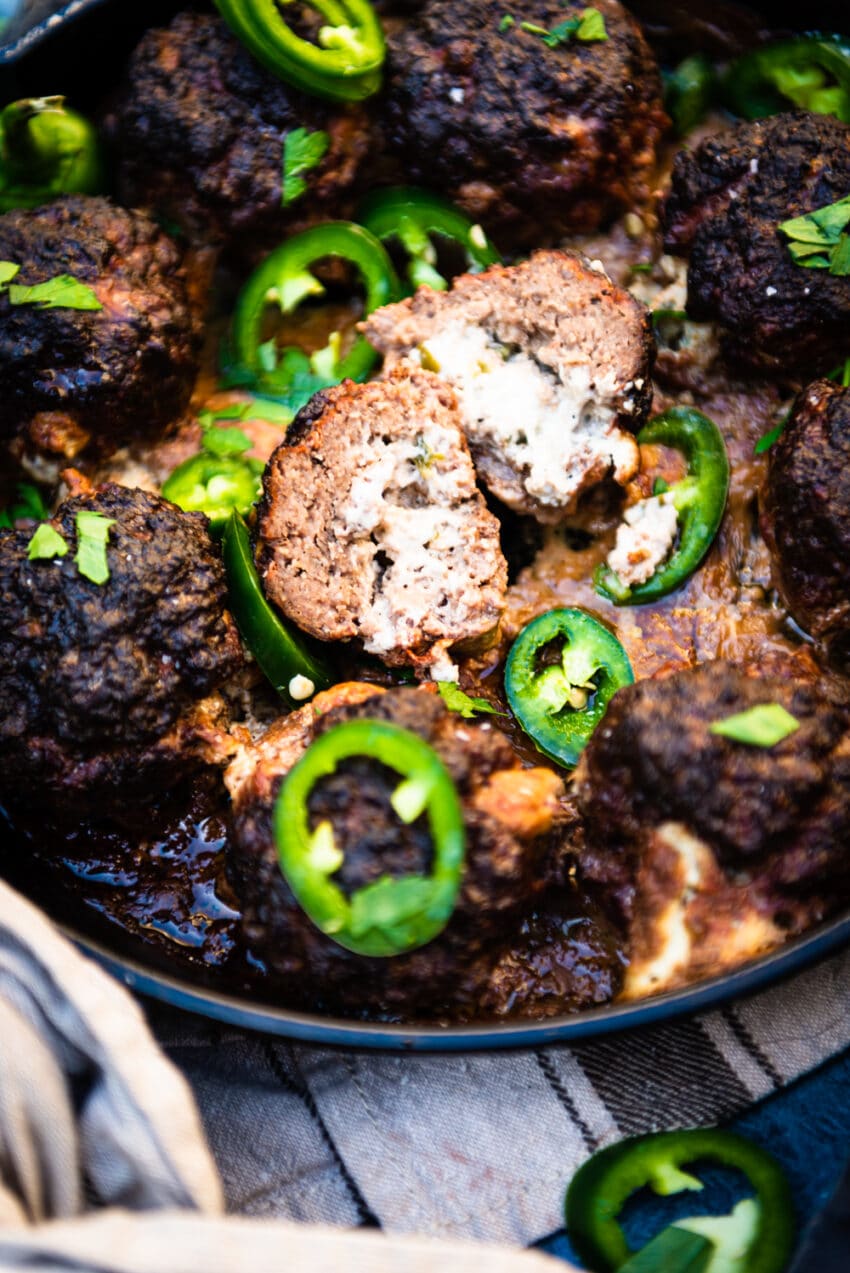 Smoked jalapeno popper meatball in skillet sliced in half to show cream cheese filling with sliced jalapenos