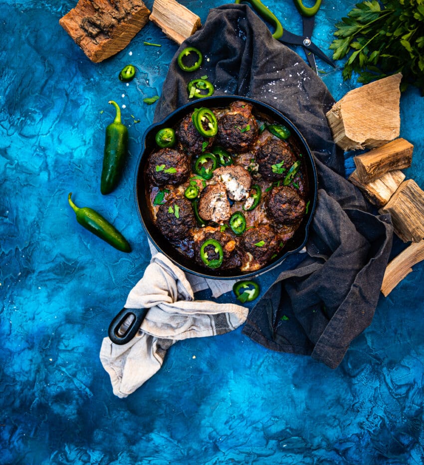 Skillet with smoked jalapeno popper meatballs with one sliced open and garnished with sliced jalapeno