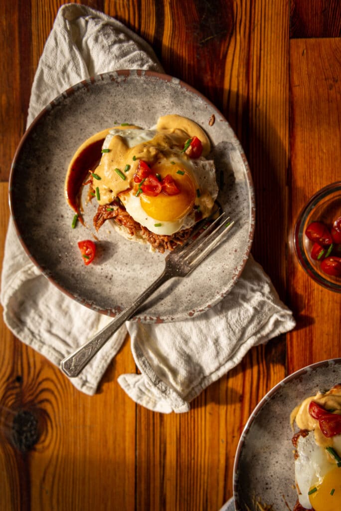 flatlay of an eggs benedict with a bbq hollandaise topped with sliced cherry tomatoes and chives