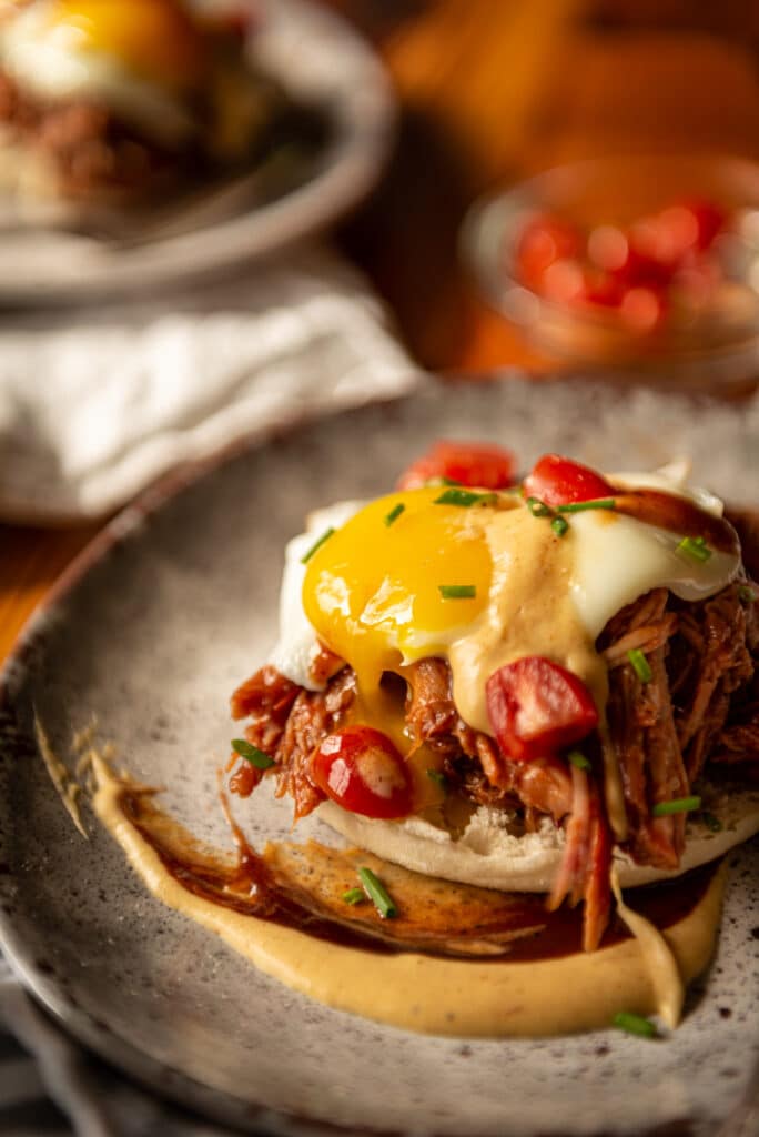 Fried egg over pulled pork and a muffin on a plate with an artiful smear of bbq sauce and bbq hollandaise sauce. 