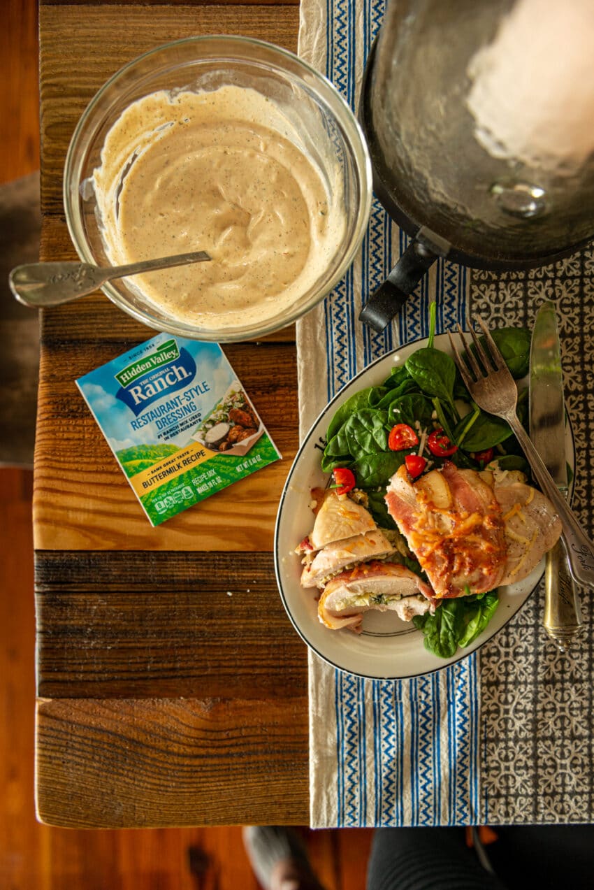 Flat lay shot over a bowl of ranch salad dressing and plated sliced bacon wrapped chicken breast