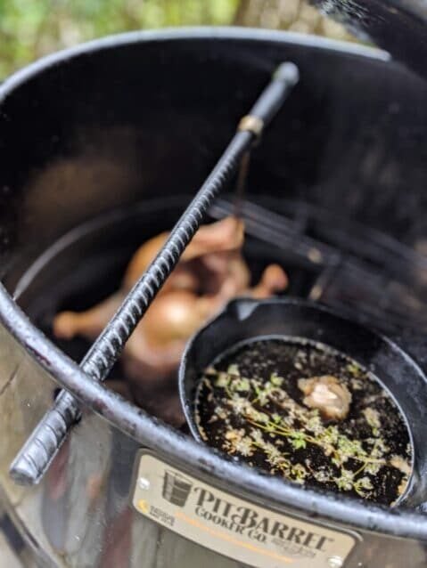 duck hanging in a smoker with cast iron skillet of basting liquid 