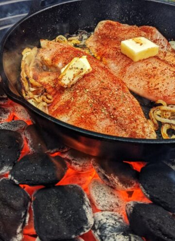 2 tilapia fillets topped with butter in cast iron skillet over hot charcoal