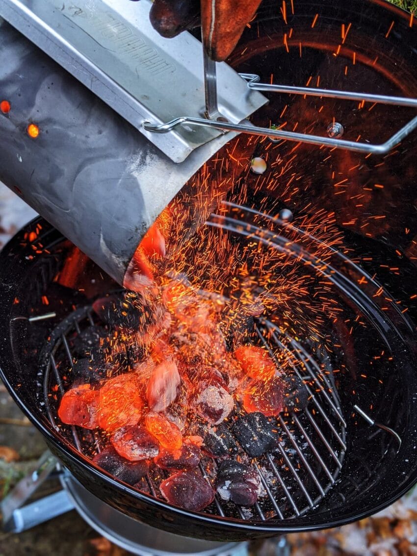 Hot coals and embers being poured from a charcoal chimney to grill