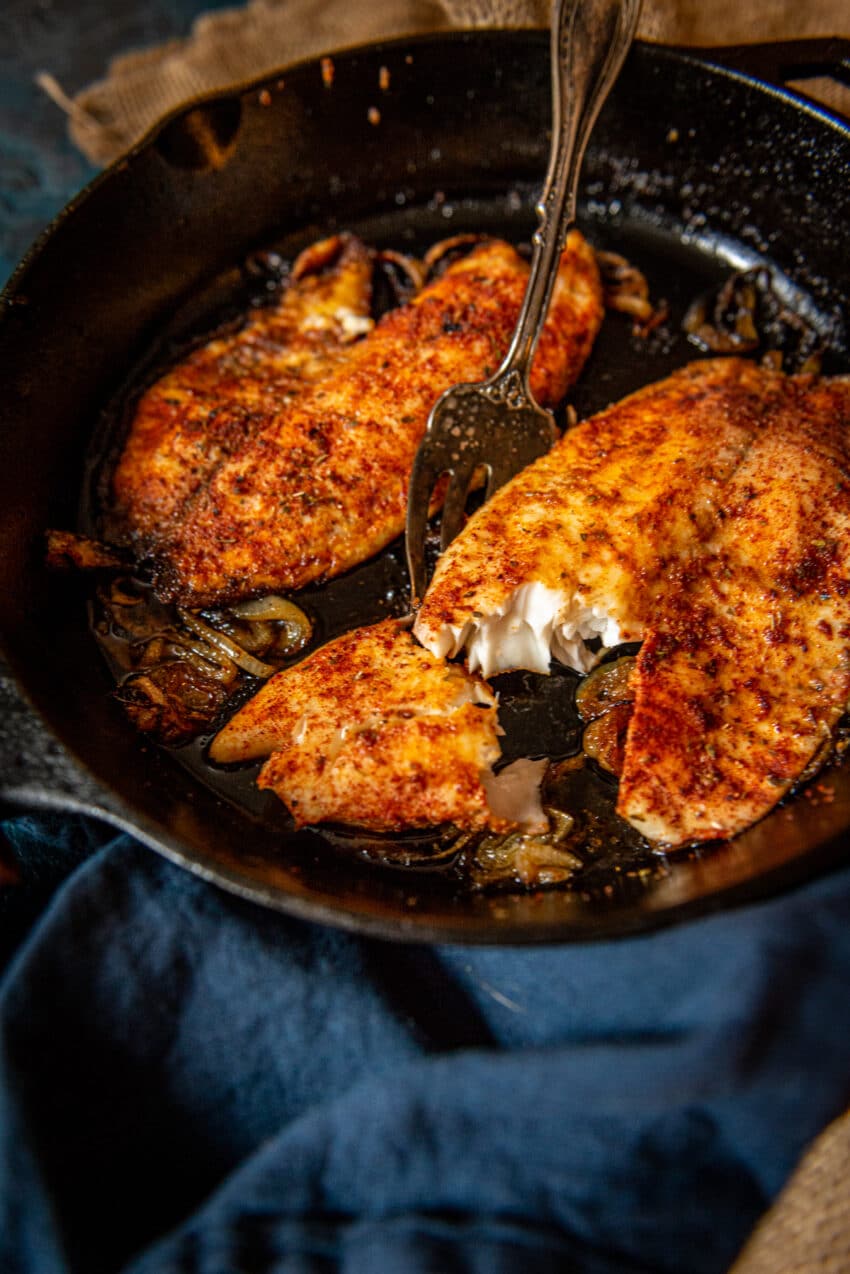 2 paprika coated cooked tilapia filets in a cast iron skillet