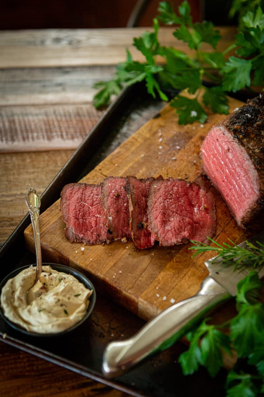 Medium-rare slices of smoked beef on a cutting board with smoked horseradish cream sauce