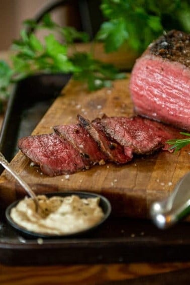 Smoked roast beef sliced on a cutting board with smoked horseradish cream sauce in a bowl and parsley in the background