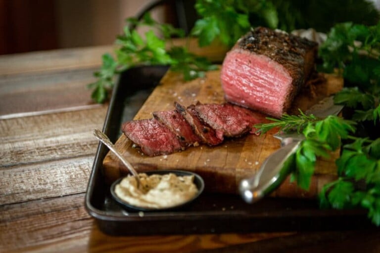 Smoked roast beef sliced on a cutting board with smoked horseradish cream sauce in a bowl and parsley in the background