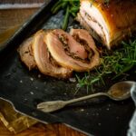 Pork loin, roasted and sliced to show mushroom and bacon stuffing on a baking sheet