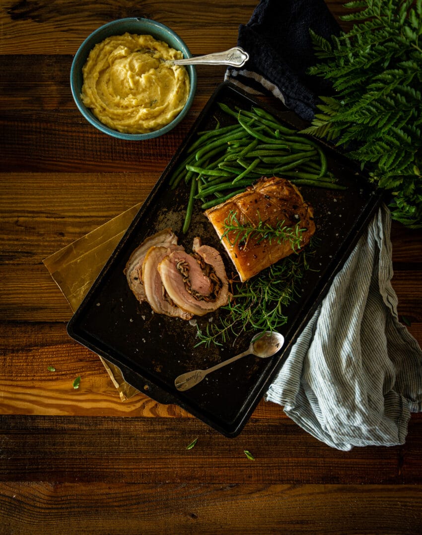 Oven roasted stuffed pork loin sliced into portions with mashed potatoes, green beans and herbs. 