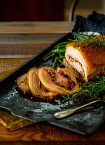 Pork loin thats been stuffed and roasted sliced and set on a table to serve with fresh green herbs