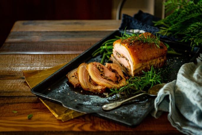Pork loin thats been stuffed and roasted sliced and set on a table to serve with fresh green herbs