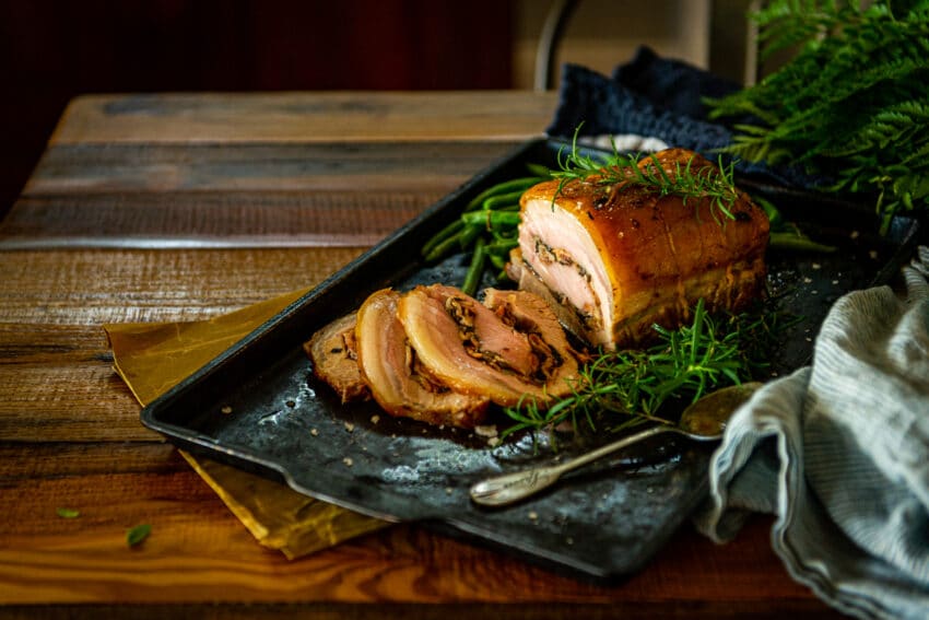 Pork loin thats been stuffed and roasted sliced and set on a table to serve with fresh green herbs.