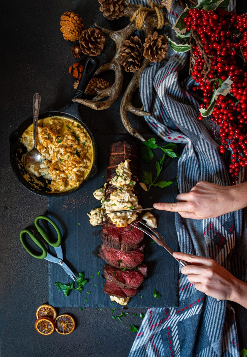 Hands slicing a smoked beef tenderloin topped with crab imperial