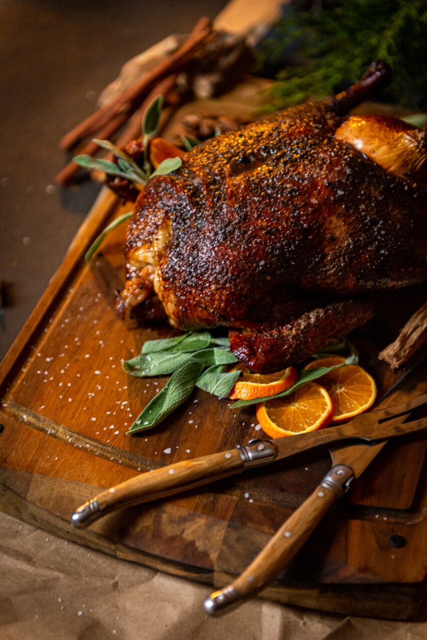 close up of smoked duck on cutting board with sage and sliced oranges