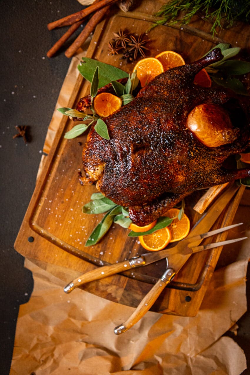 Smoked duck on a wood cutting board with sage and oranges 