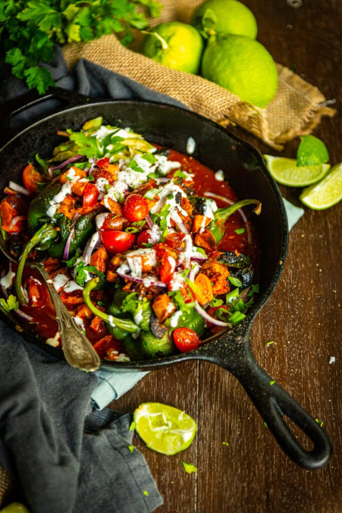 cast iron skillet filled with chicken tinga stuffed poblanos and various toppings 