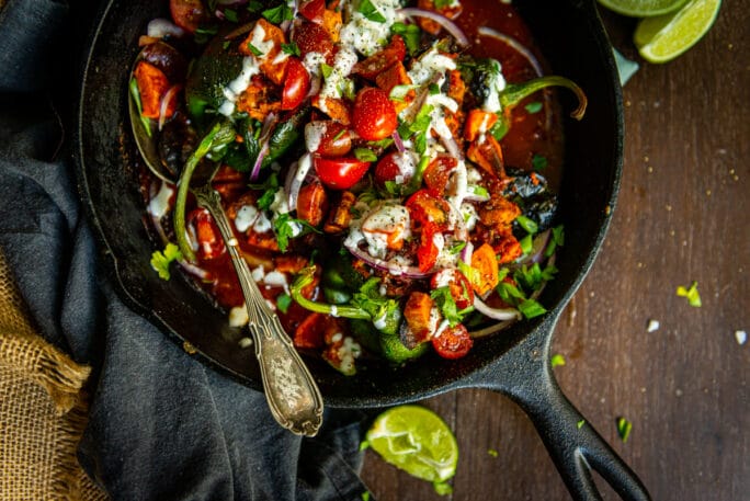 above shot showing skillet of cooked chicken tinga stuffed peppers with tomatoes, crema and limes