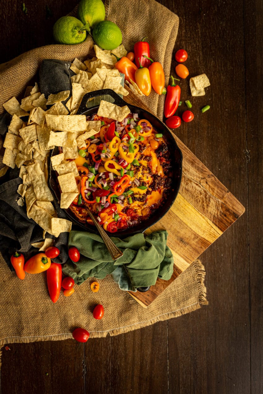 Chorizo cheese dip in a skillet covered in crisp sliced veggies with chips to dip - all just waiting to be eaten!