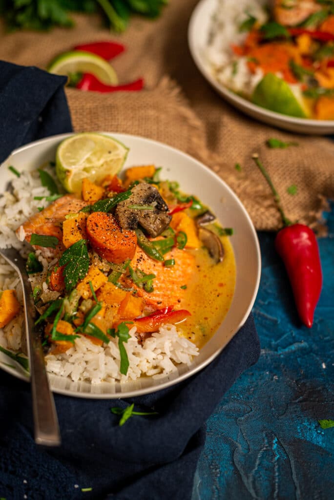 Close up of quick salmon curry in a white bowl showing rice topped with salmon and creamy coconut curry loaded with veggies